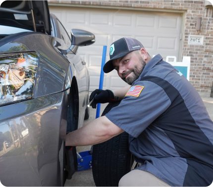Photograph of smiling Goodhood mobile mechanic fixing a vehicle in front of a Dallas home